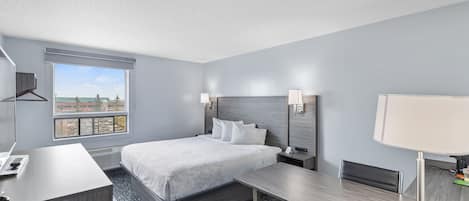 Ett modernt hotellrum med en säng, ett skrivbord och ett stort fönster med utsikt över stadsbilden.