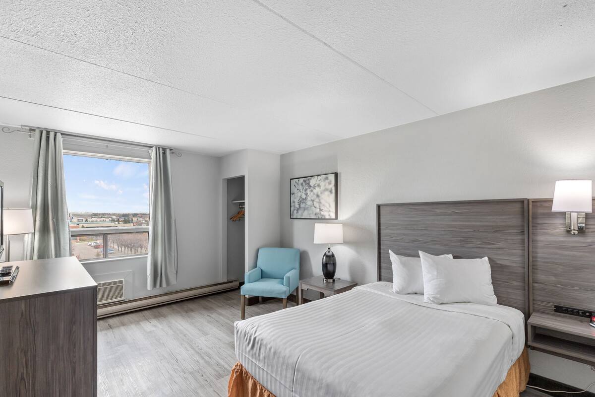 Une chambre d’hôtel avec un grand lit, un bureau, une chaise, une table de chevet et une fenêtre avec des rideaux.
