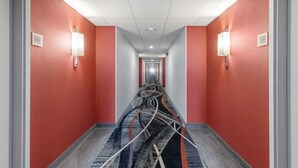 Un couloir d’hôtel aux murs rouges, au plafond blanc et au tapis orné de motifs abstraits.