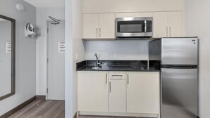Une cuisine de taille réduite, avec des meubles de couleur claire, un four à micro-ondes en acier inoxydable et un réfrigérateur.