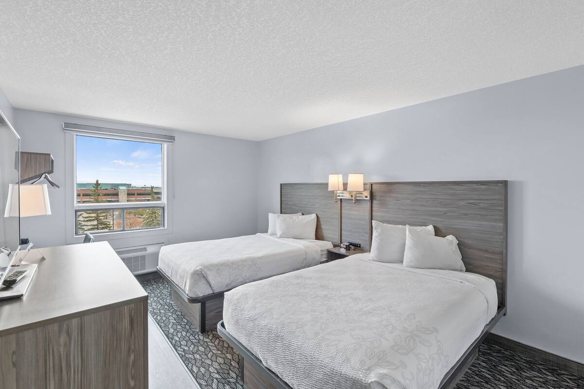 Une chambre d’hôtel avec deux lits, un bureau et une grande fenêtre donnant sur la ville.