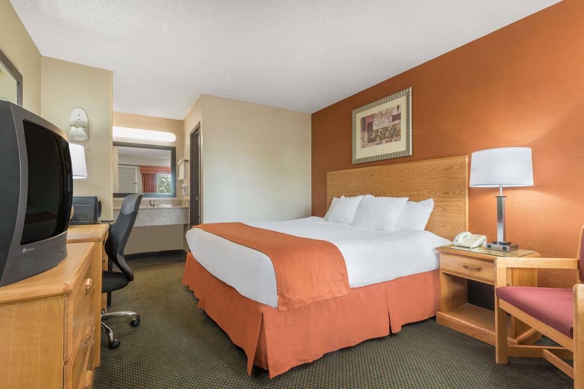 Een hotelkamer met een bed, een bureau met een computer, een stoel, een lamp en een telefoon.