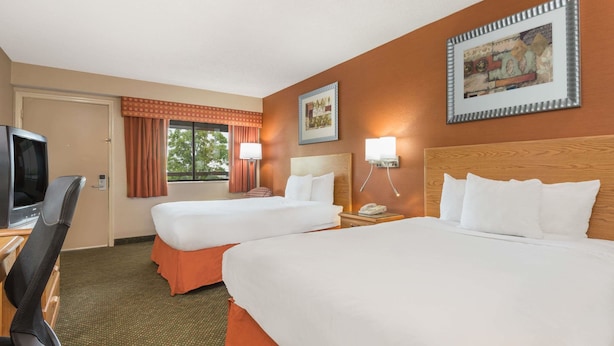 A hotel room with two beds, a desk with a TV, and a window with curtains.