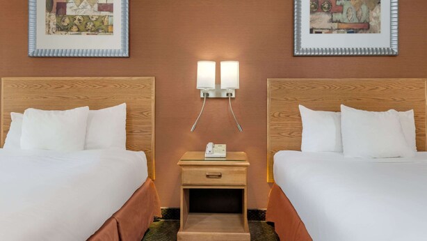 A hotel room with two beds, a nightstand with a phone, and two wall-mounted lamps. - Days Inn by Wyndham Columbus Fairgrounds (Columbus)