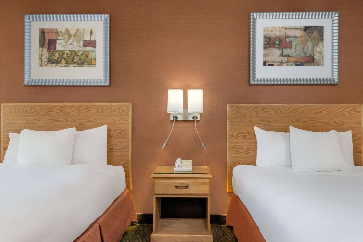 Een hotelkamer met twee bedden, een nachtkastje met een telefoon en twee wandlampen.