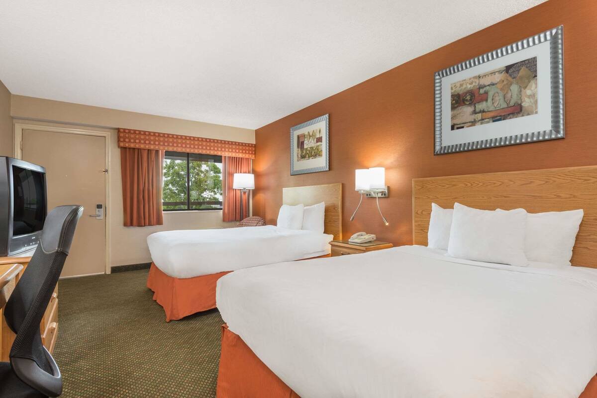 Een hotelkamer met twee bedden, een televisie, een bureau en een raam met gordijnen.