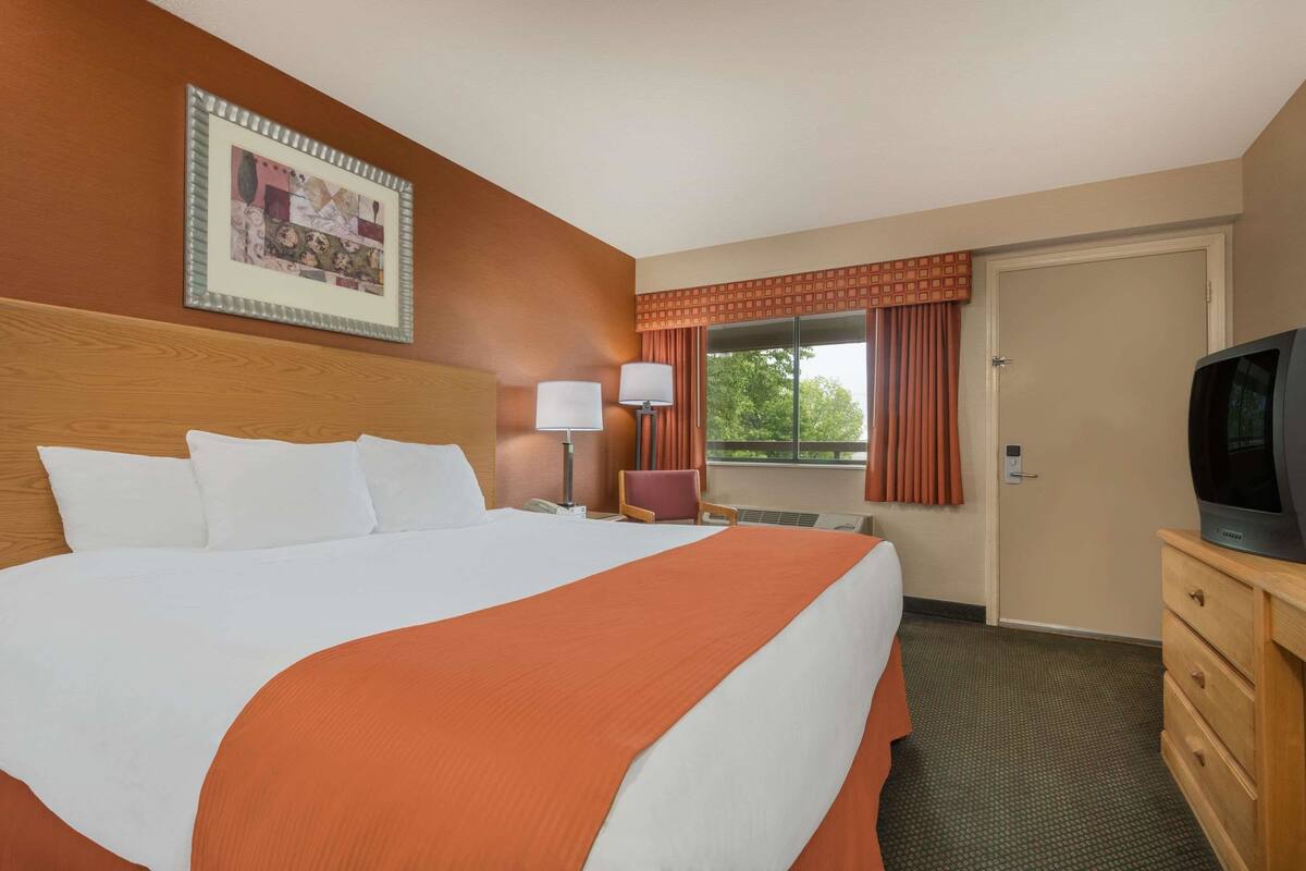 Een hotelkamer met een groot bed, een televisie, een bureau en een raam met gordijnen.