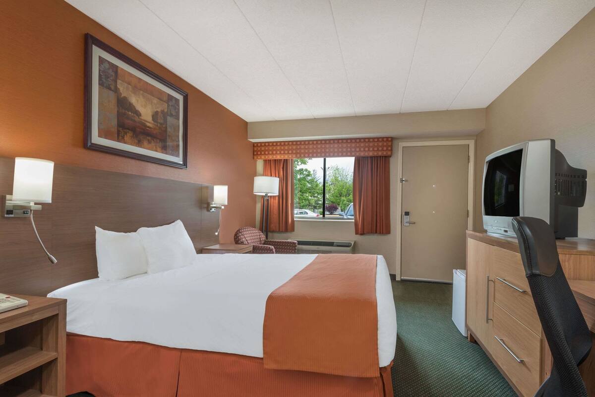 Een hotelkamer met een groot bed, een televisie, een bureau met een lamp, een stoel en een schilderij aan de muur.