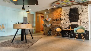 Un intérieur moderne avec un mur décoré d’une fresque en briques, une table ronde en bois et deux chaises.
