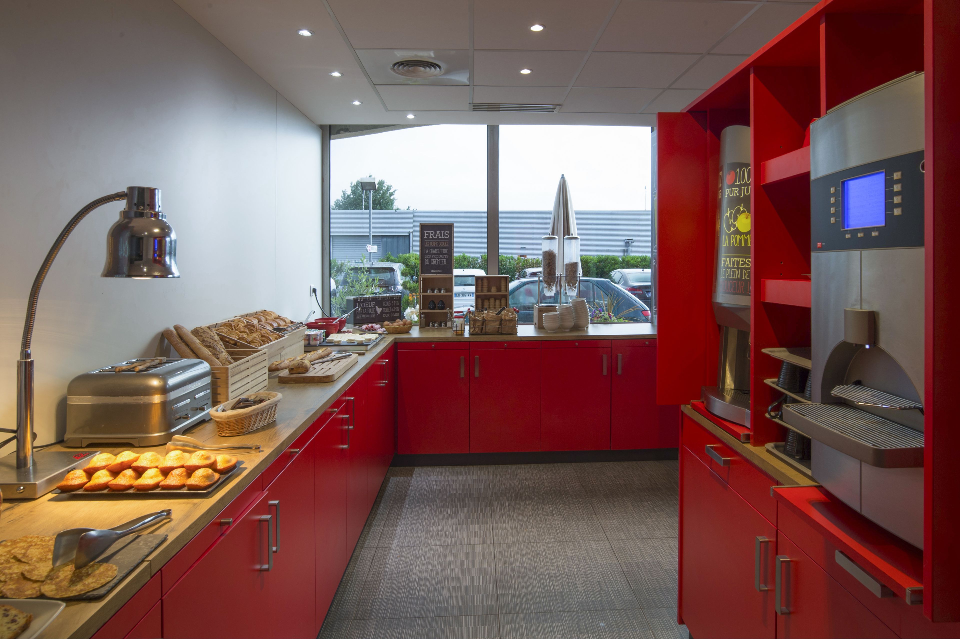 Een keuken met rode kastjes, een broodrooster, een broodvitrine en een koffieapparaat.