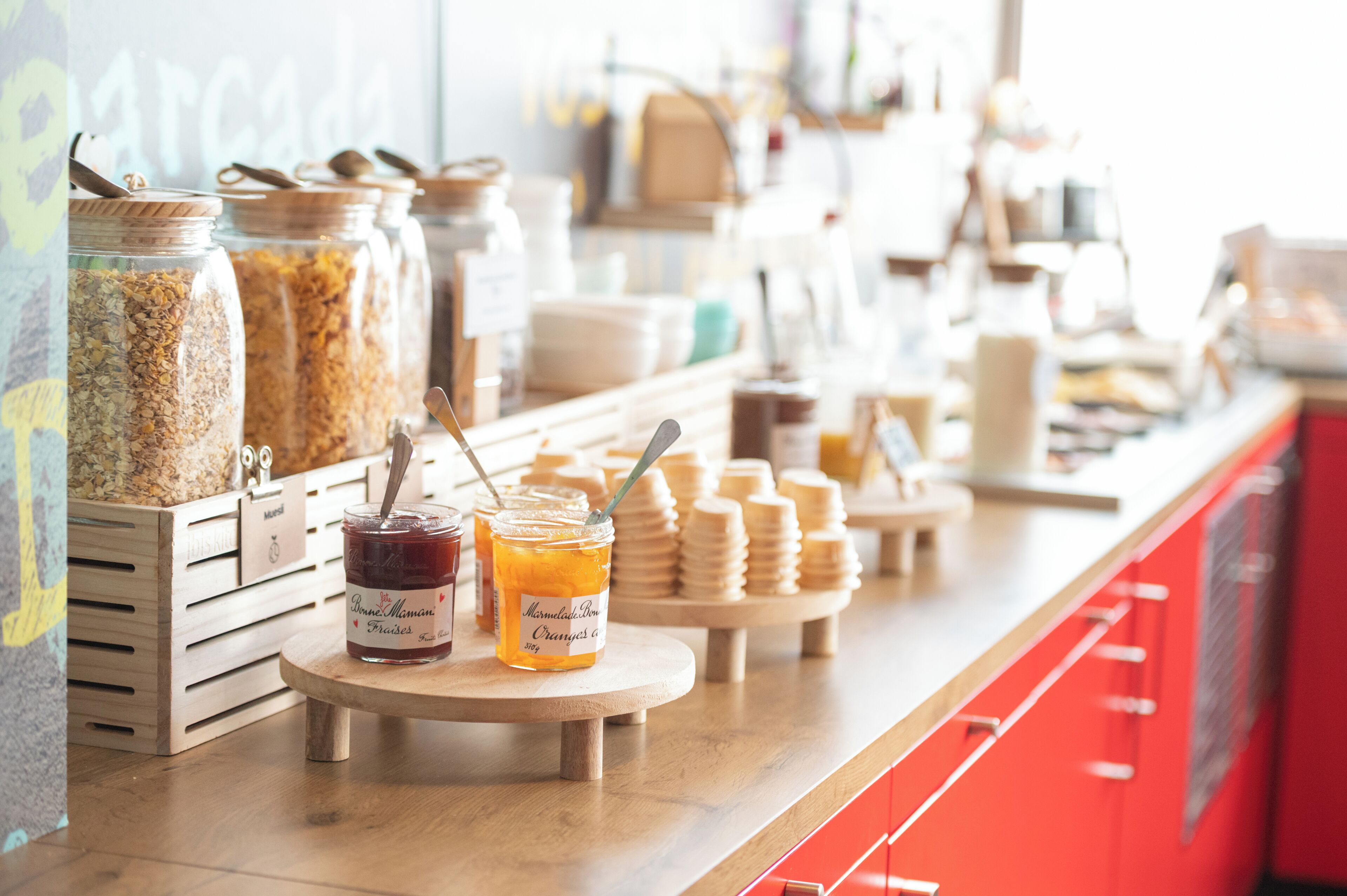 A buffet counter with jars of spreads and a wooden stand with stacked plates.