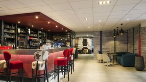 Un espace bar doté d’un long comptoir, de chaises rouges et blanches, et d’un coin salon avec des canapés et des tables.