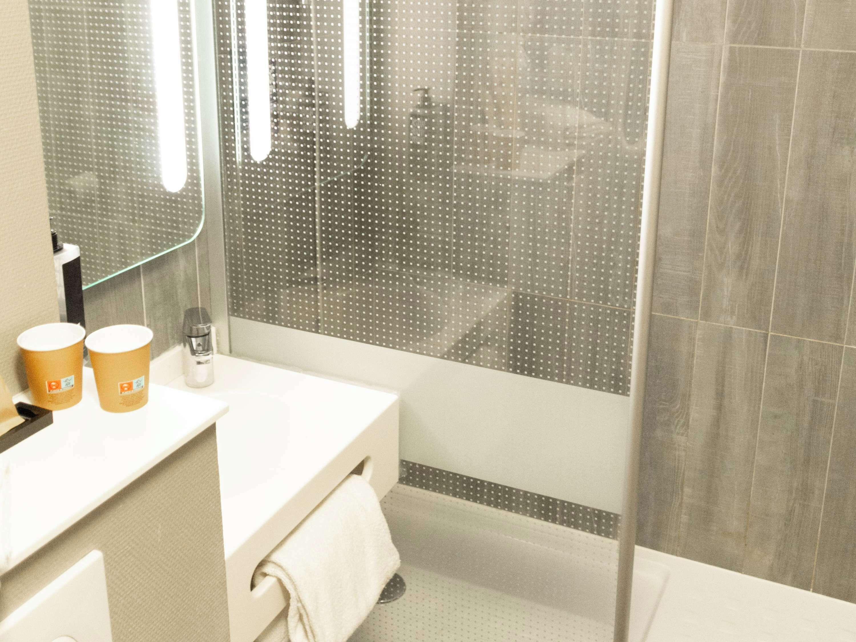 A modern bathroom with a white sink, two paper towel dispensers, a mirror, and a shower area with a glass door.