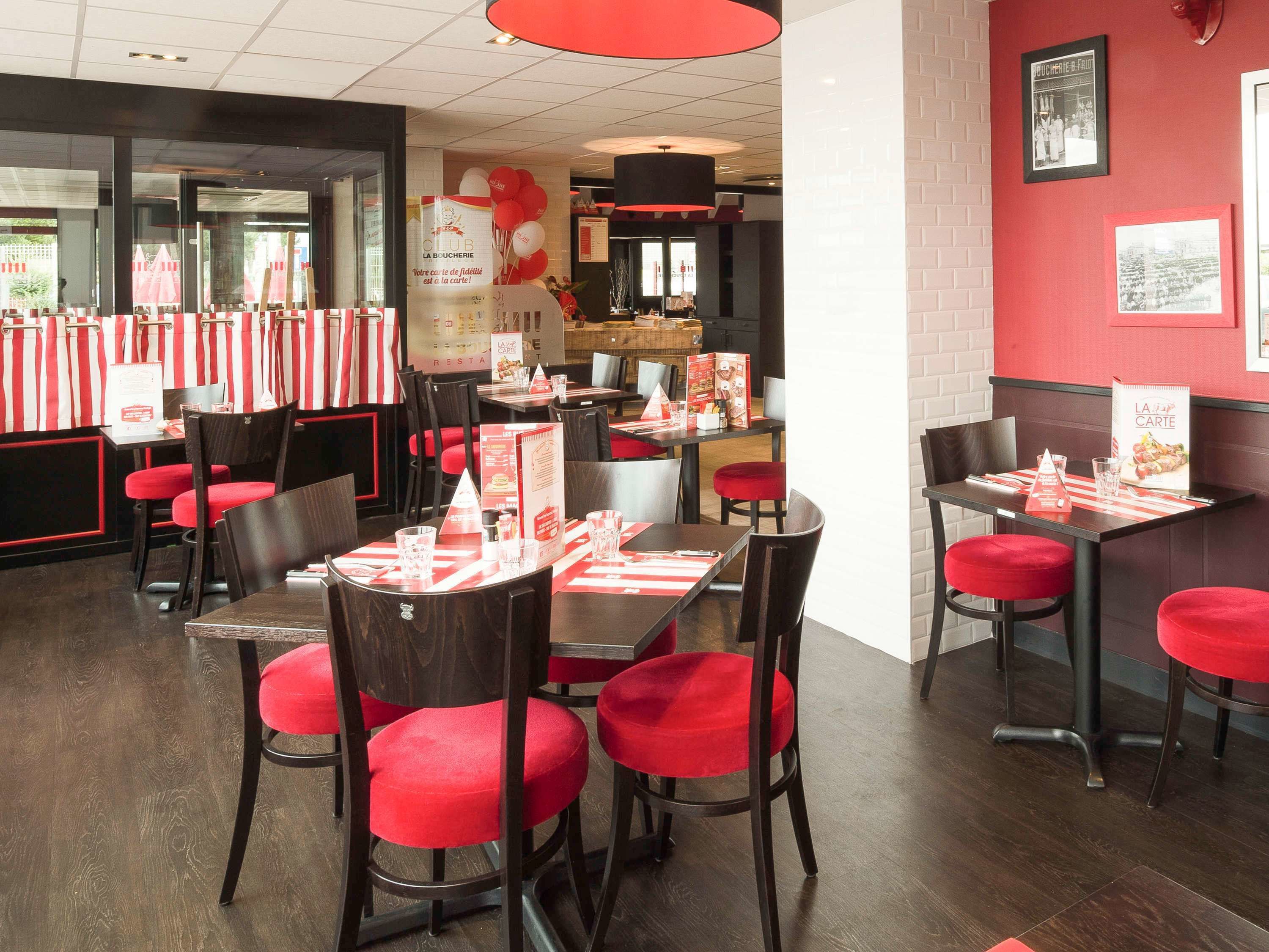 Interior de restaurante con mesas y sillas a rayas rojas y blancas, una zona de barra y una pared de ladrillo rojo con cuadros enmarcados.