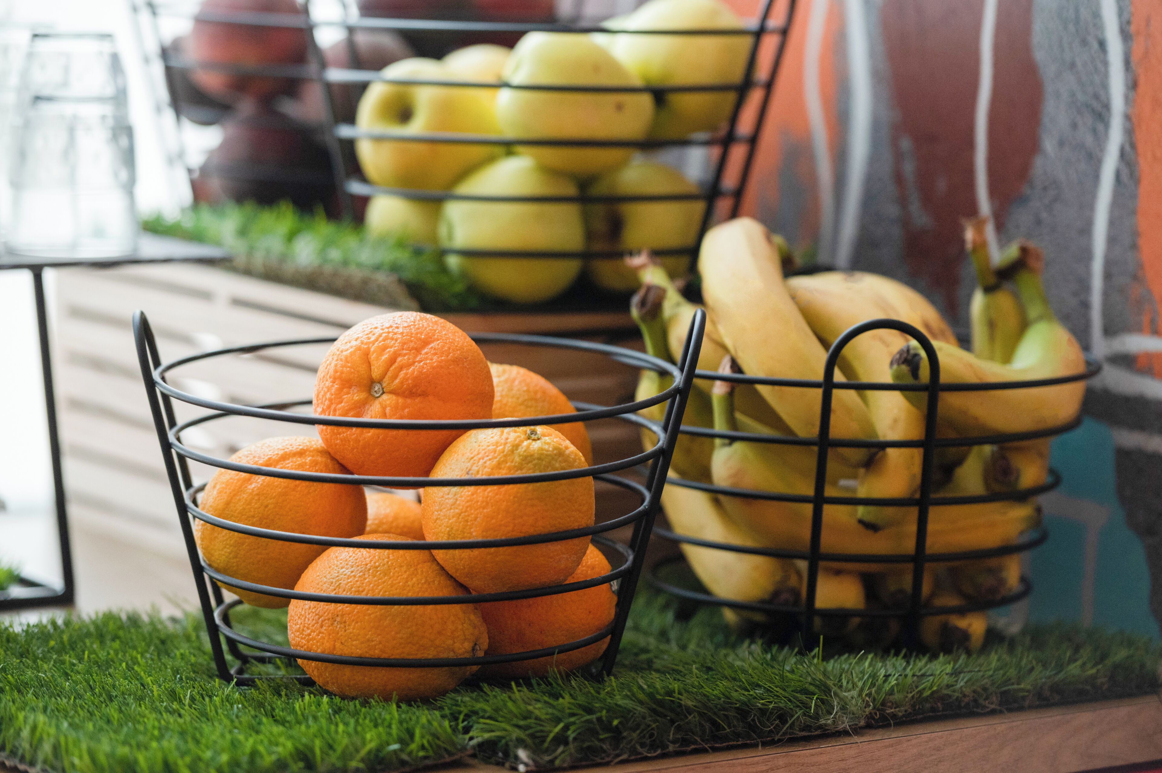 Eine Metallobstschale, gefüllt mit Orangen und Bananen, auf einer Holzoberfläche vor grünem Gras.