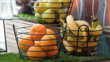 Eine Metallobstschale, gefüllt mit Orangen und Bananen, auf einer Holzoberfläche vor grünem Gras.