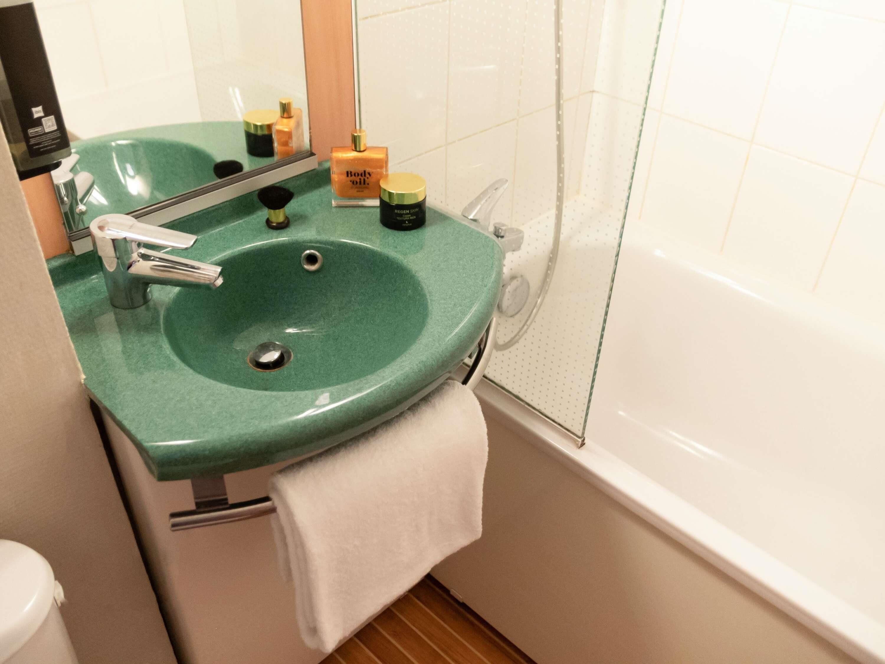 A bathroom with a green sink, a mirror, a white towel, and a bathtub.