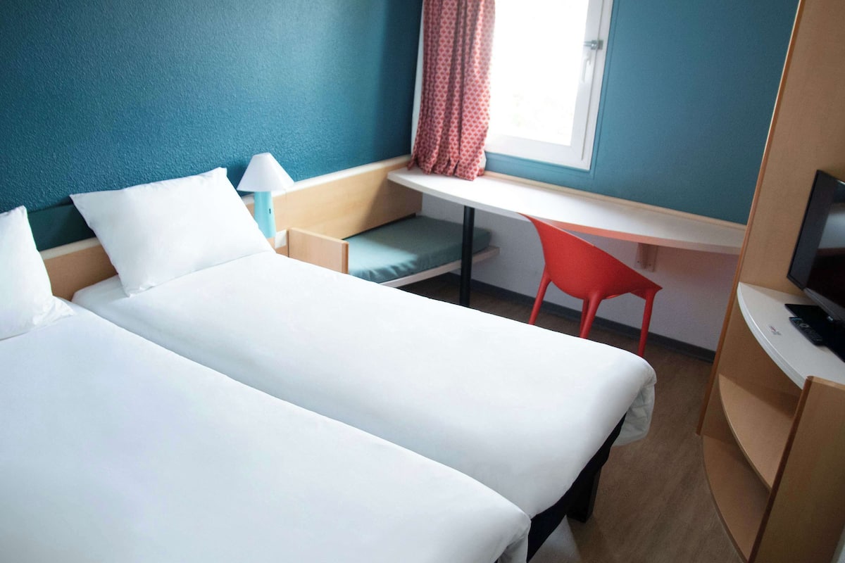 Two spacious beds with white linens, a convenient workspace, and a mounted television for entertainment.