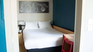 Une chambre d’hôtel équipée d’un lit, d’un bureau, d’une chaise, d’une lampe et d’un climatiseur fixé au mur.