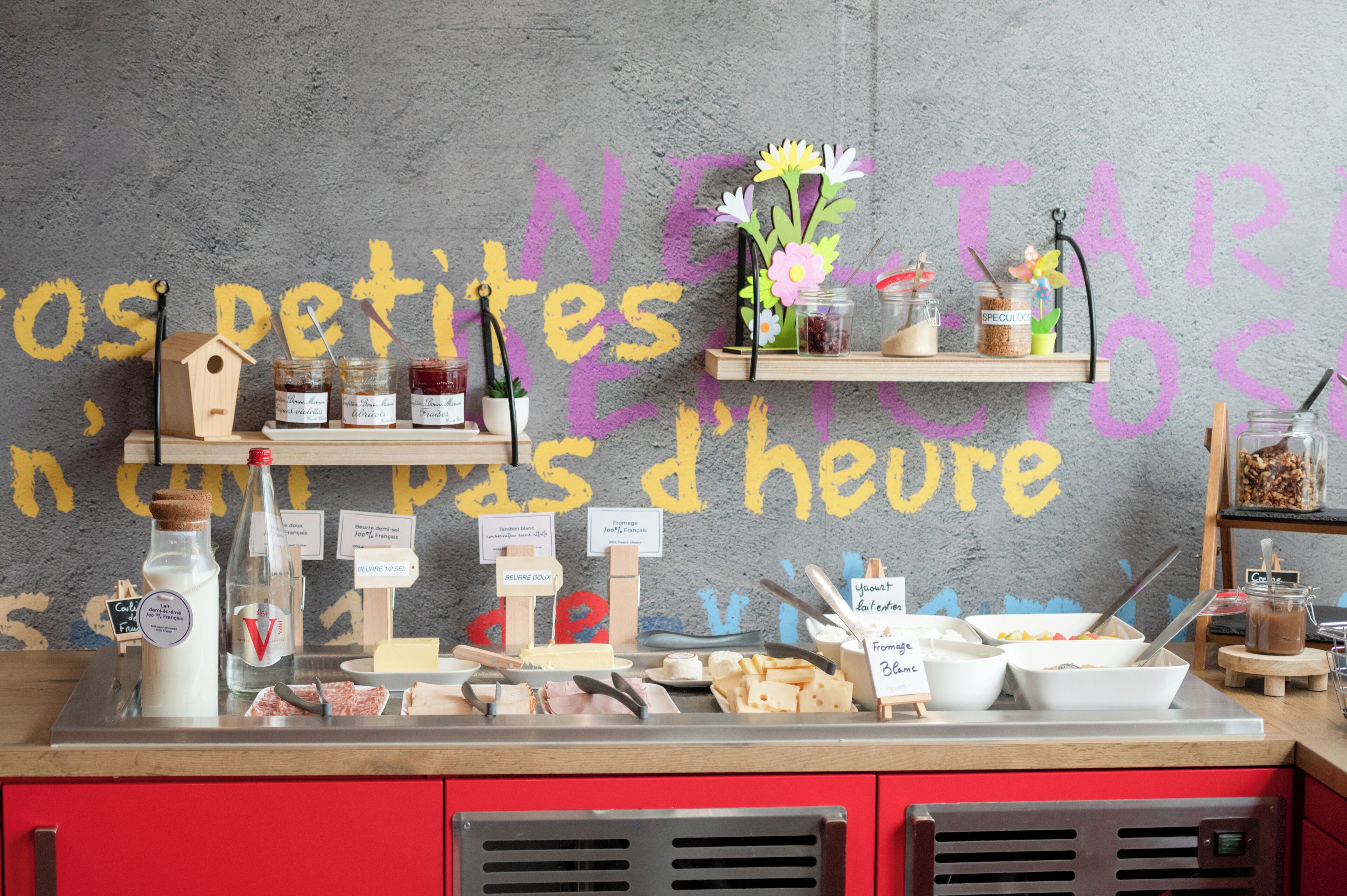 Un buffet pour le petit-déjeuner proposant divers aliments et accompagnements, notamment des pots de confiture, une bouteille de lait et une mangeoire à oiseaux en bois.