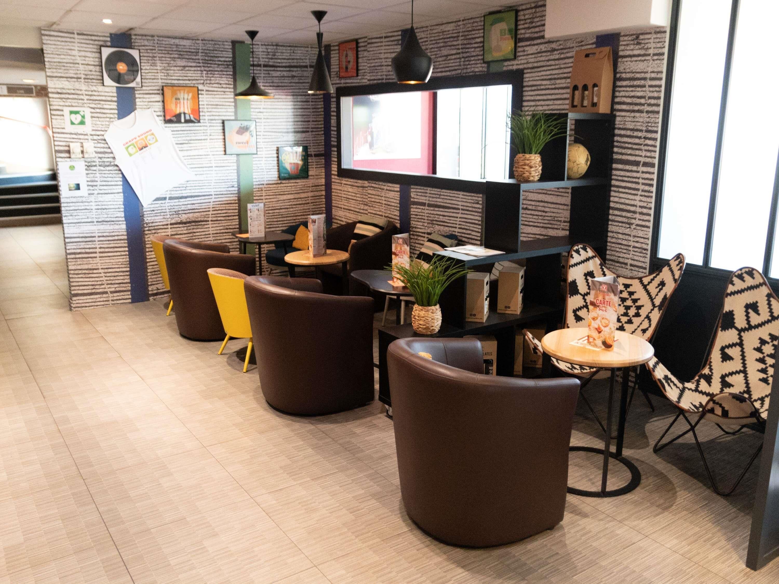 A modern cafe with round tables and chairs, a large screen, and a patterned wall.