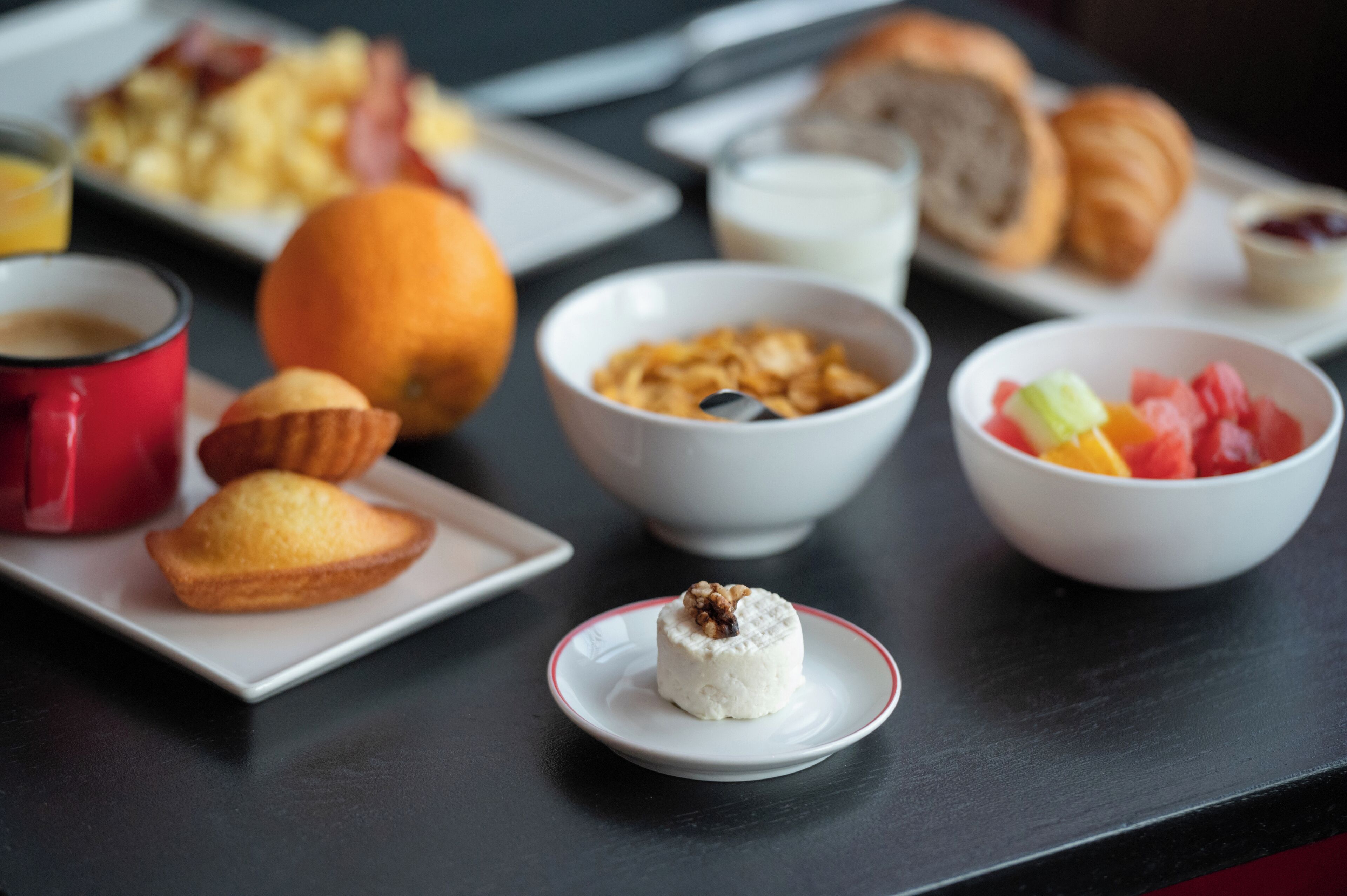 Une table de petit-déjeuner avec divers aliments, notamment un muffin, un croissant et un bol de fruits.