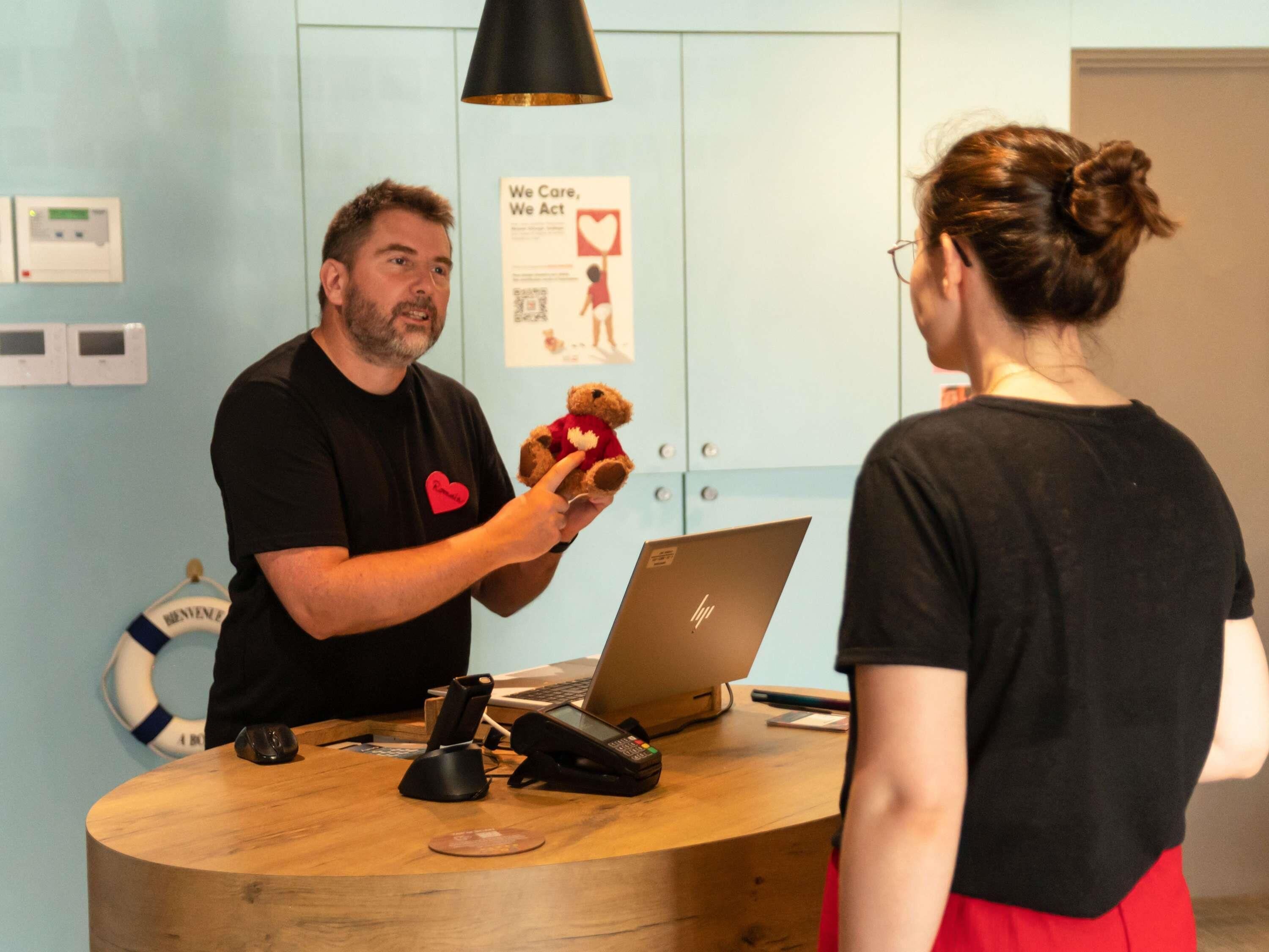 A reception desk with a laptop, a telephone, and a teddy bear.