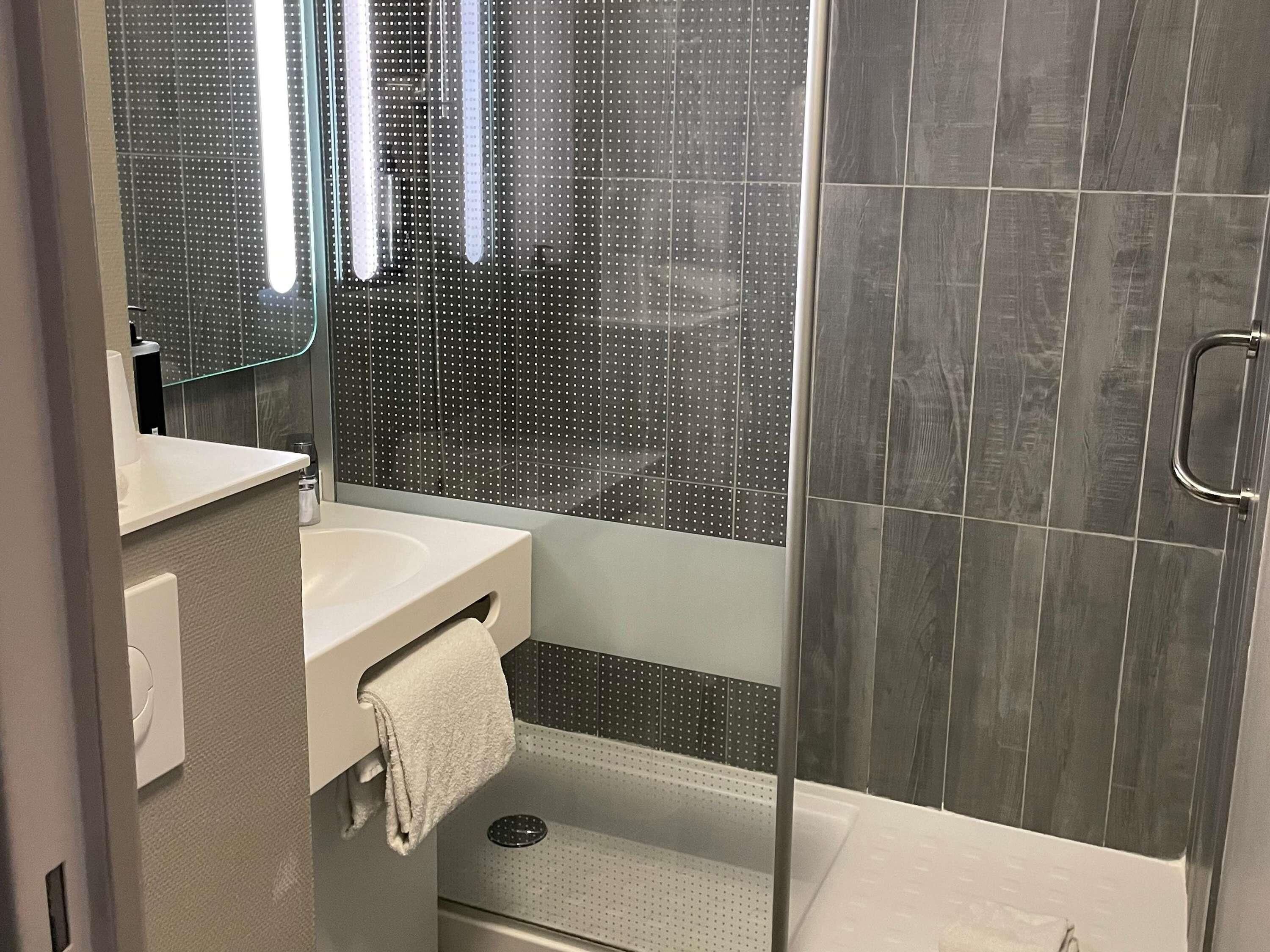 A modern bathroom with a glass shower enclosure, a white sink, and a towel rack.