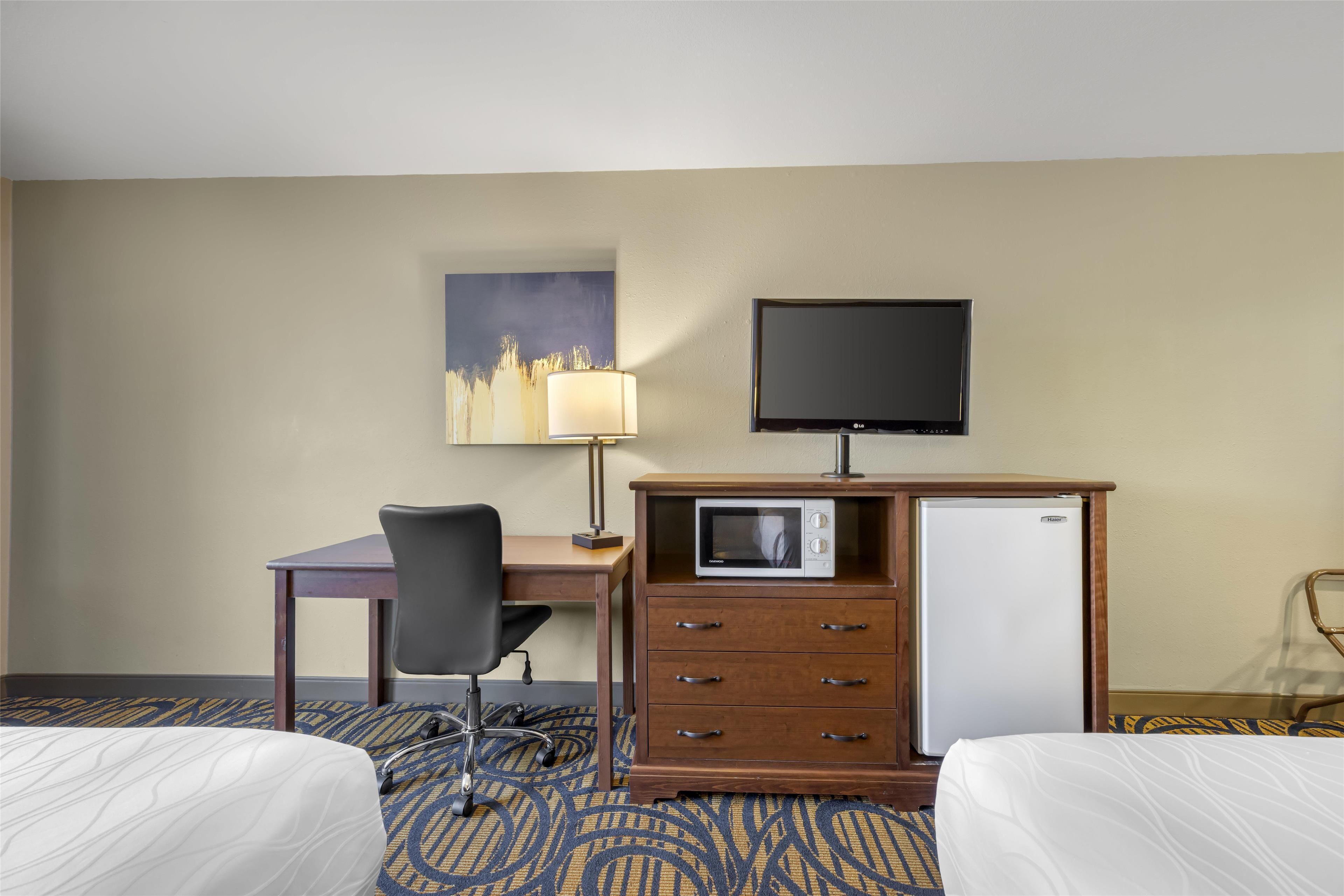 A hotel room with two beds, a desk with a chair, a television, a microwave, and a refrigerator.