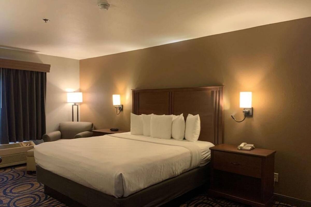 Una habitación de hotel con una cama grande, lámparas de noche, un escritorio y una silla.