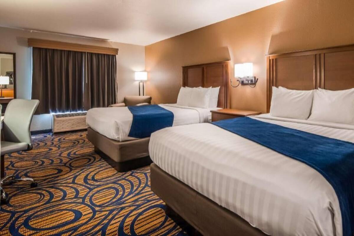 Habitación de hotel con dos camas, un escritorio, una silla y una alfombra grande con motivos.