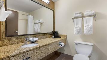 Un baño con lavamanos de encimera de granito, un espejo, un inodoro y toalleros.