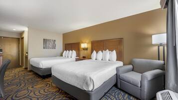 A hotel room with two beds, a desk, a chair, and a lamp.
