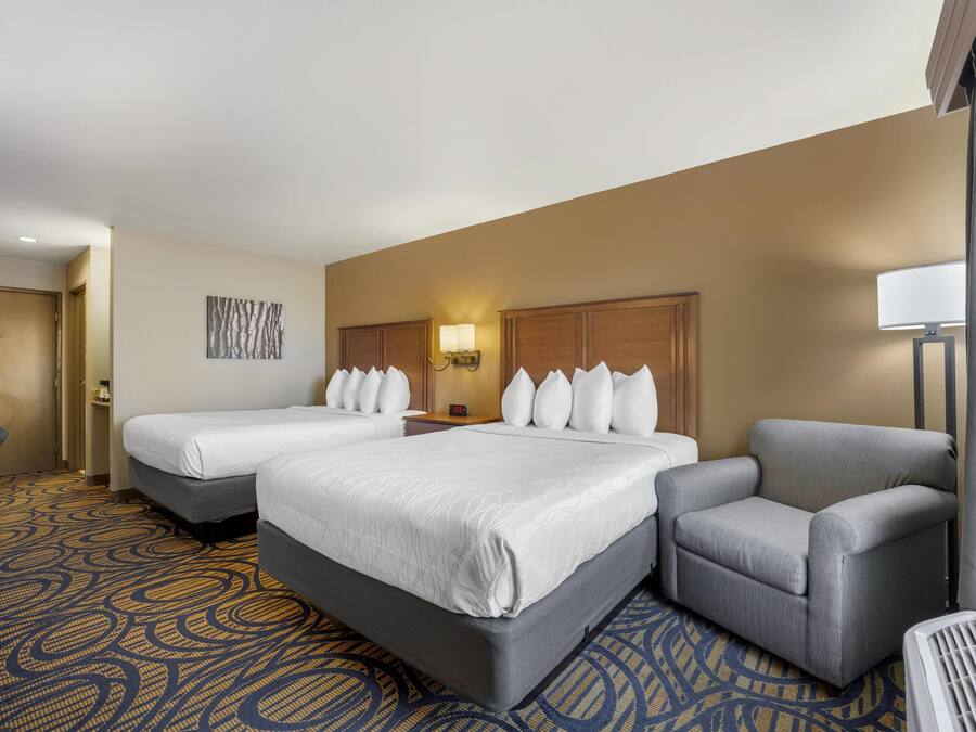 A hotel room with two beds, a desk, a chair, and a lamp.