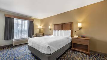 A hotel room with a large bed, two bedside lamps, a nightstand, a chair, and a window with curtains.