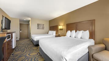 A hotel room with two beds, a desk with a television, and a patterned carpet.