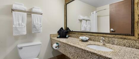 A bathroom with a white toilet, a sink with a granite countertop, a mirror, and two towel racks with white towels.
