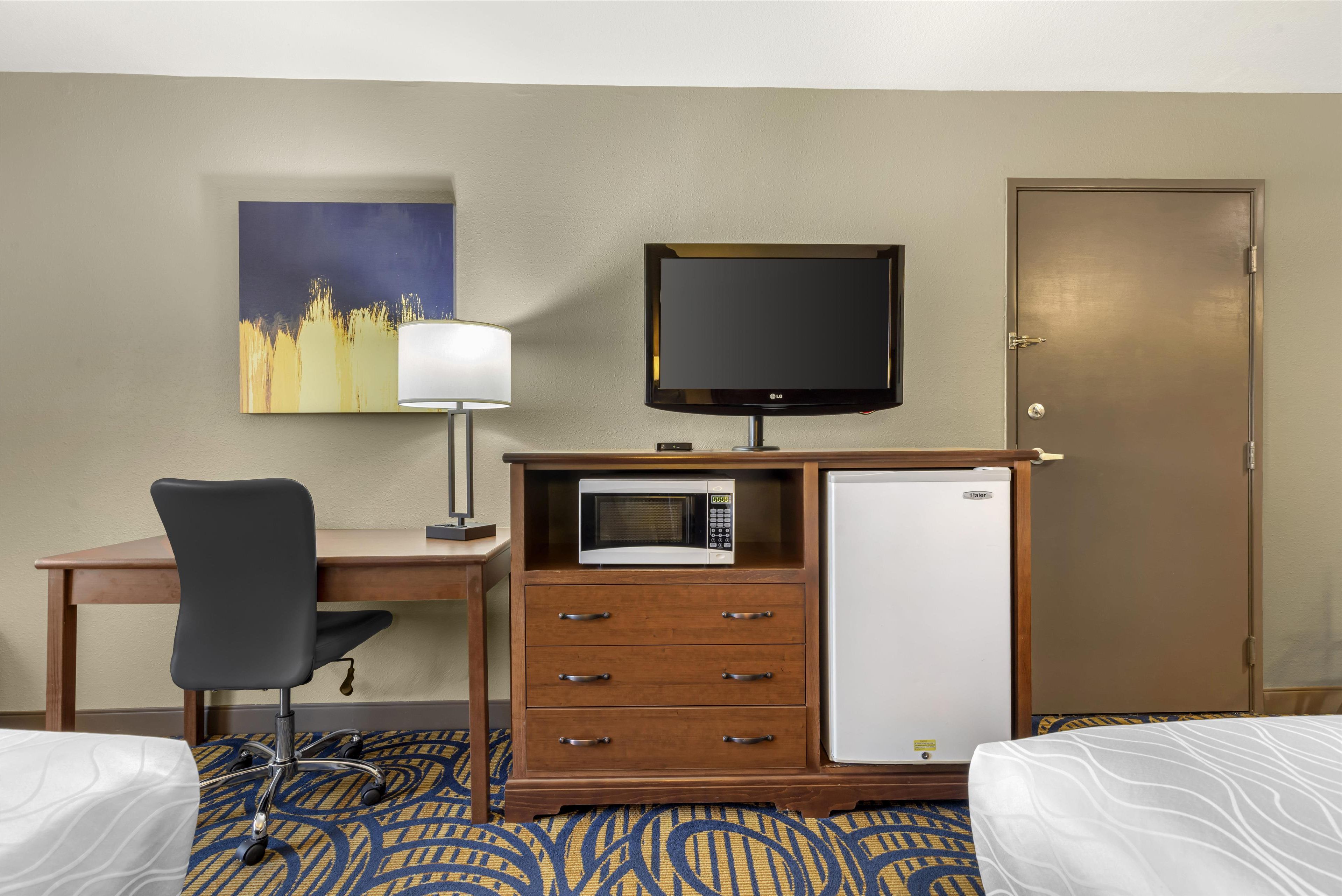 Habitación de hotel con cama, escritorio con silla, televisión, microondas y refrigerador.