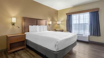 Een hotelkamer met een groot bed, een houten nachtkastje, twee wandlampen, een raam met gordijnen en een airconditioning.