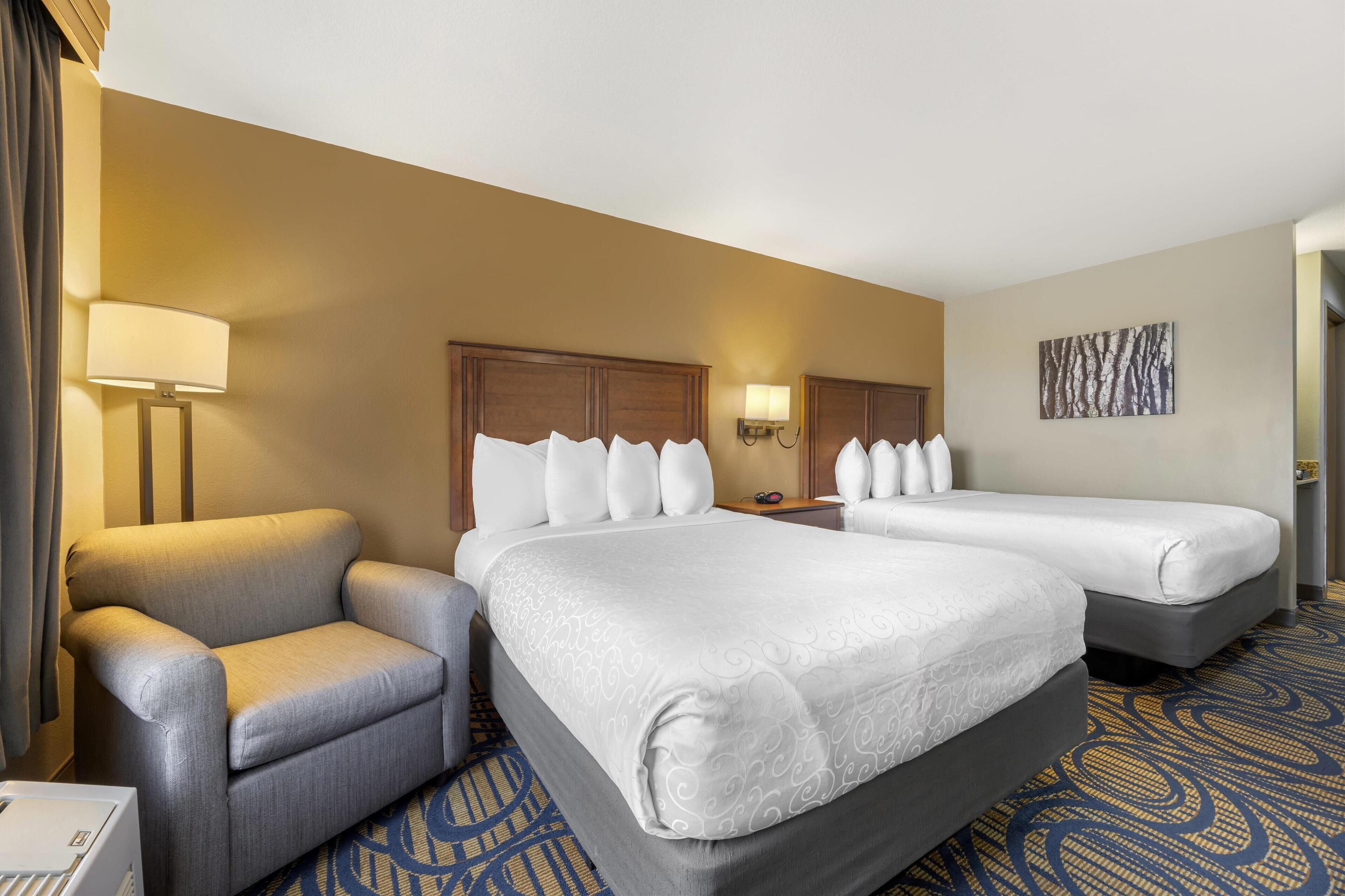 A hotel room with two beds, a sofa, a lamp, and a painting on the wall.