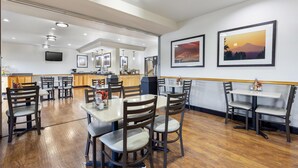Un restaurante con suelo de madera, varias mesas y sillas, una barra y cuadros en la pared.