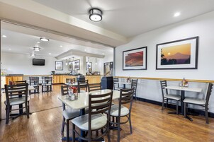 A restaurant with wooden flooring, multiple tables and chairs, a counter, and framed pictures on the wall.