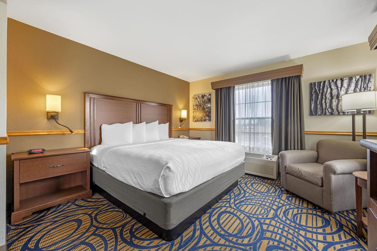 Una habitación de hotel con una cama grande, un escritorio, una silla, una ventana con cortinas y una lámpara de pared.