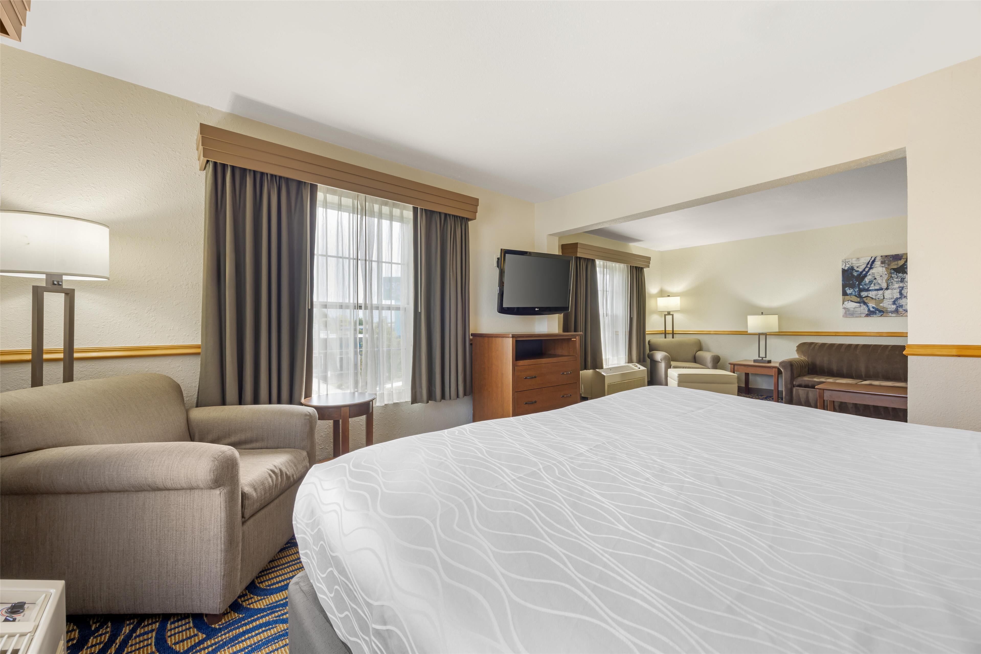 A hotel room with a large bed, a sofa, a television, and a desk with a lamp.
