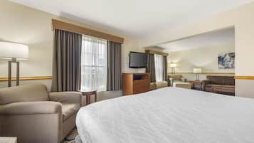 A hotel room with a large bed, a sofa, a television, and a desk with a lamp.