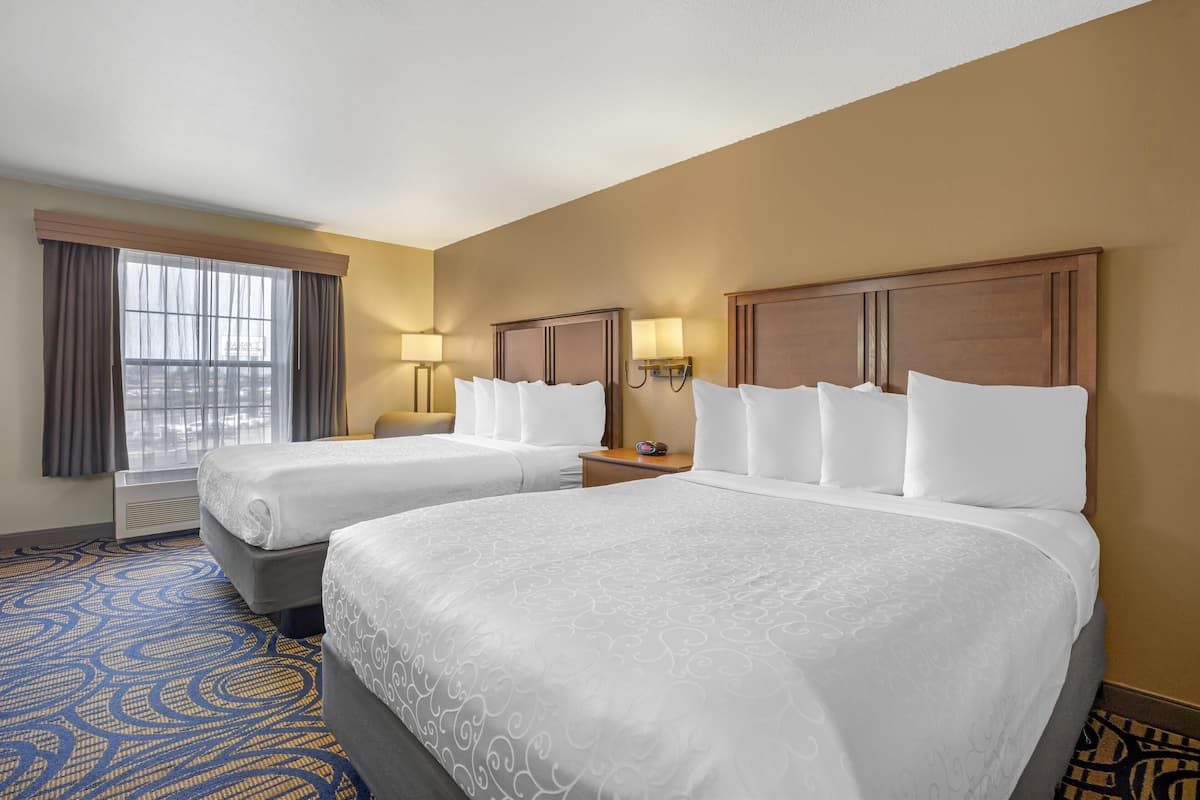 Una habitación de hotel con dos camas, un ventanal con cortinas y una alfombra estampada.