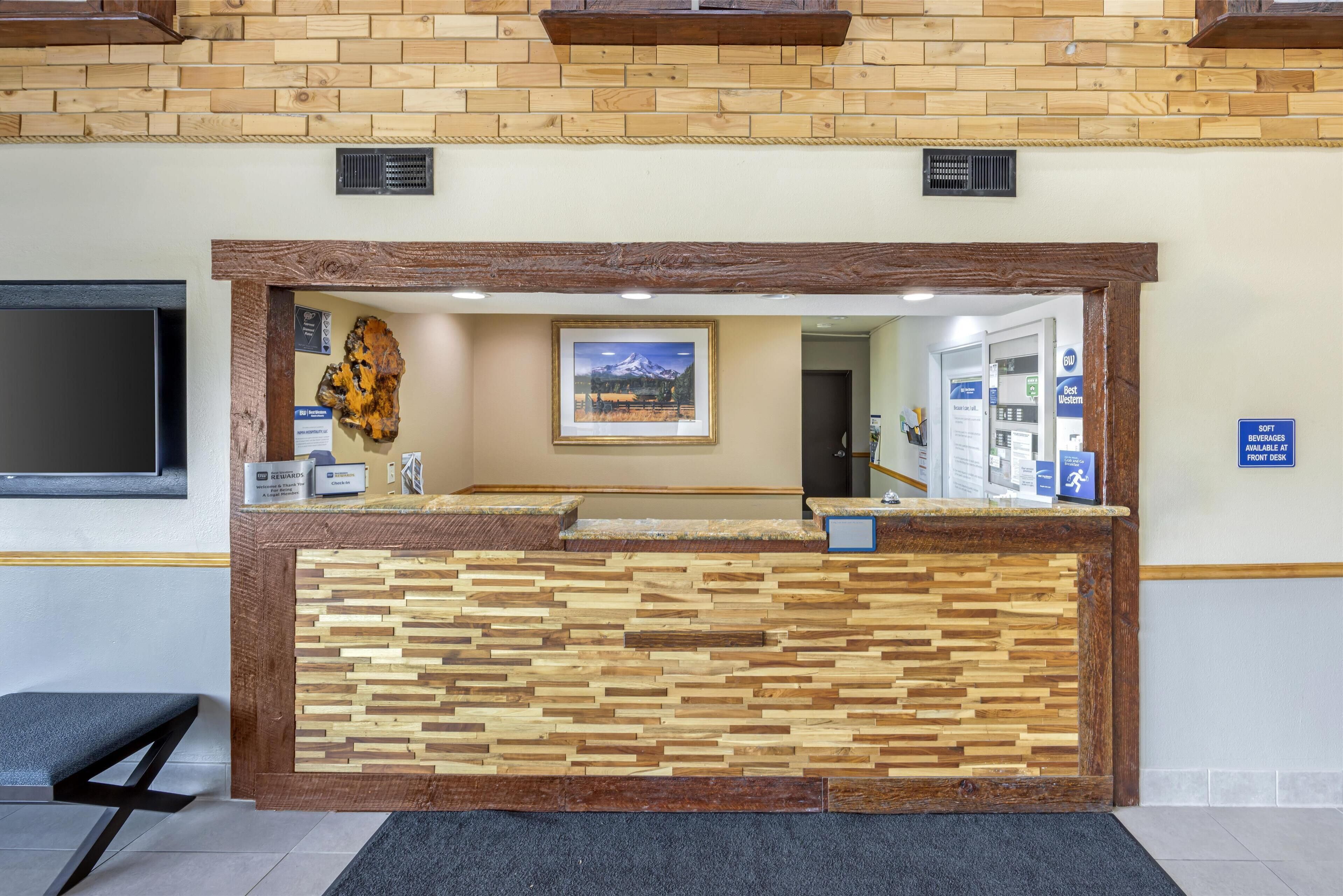 A reception desk with a wooden design, a mounted picture, and a sign indicating a soft drinks area.