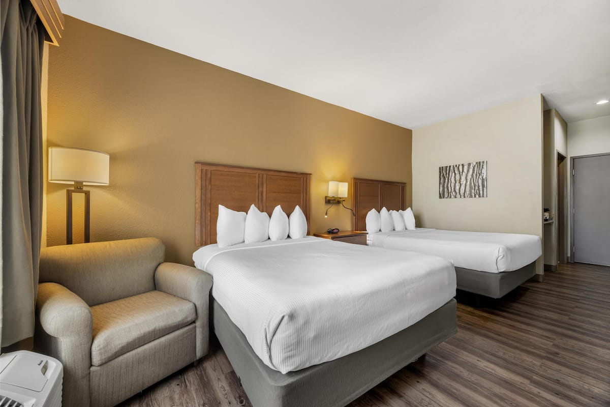 Habitación de hotel con dos camas, un sofá, una lámpara y un cuadro en la pared.