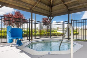 A covered swimming pool with a metal railing, a blue lifeguard chair, and a clear view of the surrounding greenery and trees.