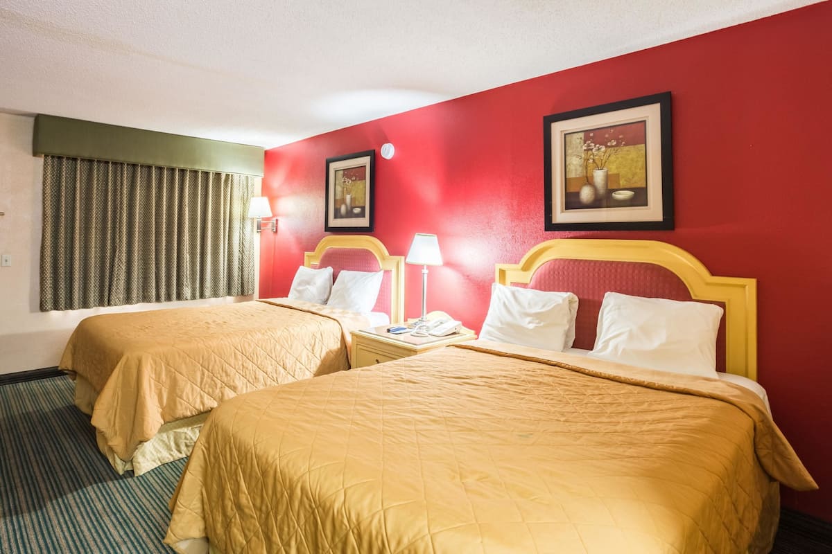 A hotel room with two beds, each with a headboard and a bedside table with a lamp.